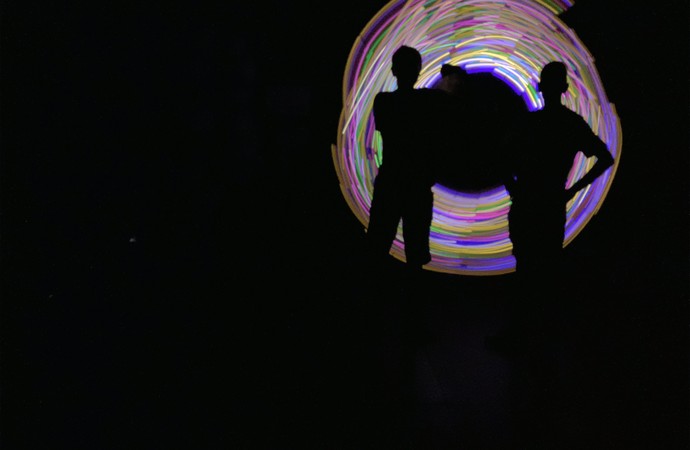Zwei Schüler:innen stehen im Dunkeln vor einem Lichtspiel aus verschiedenen Farben